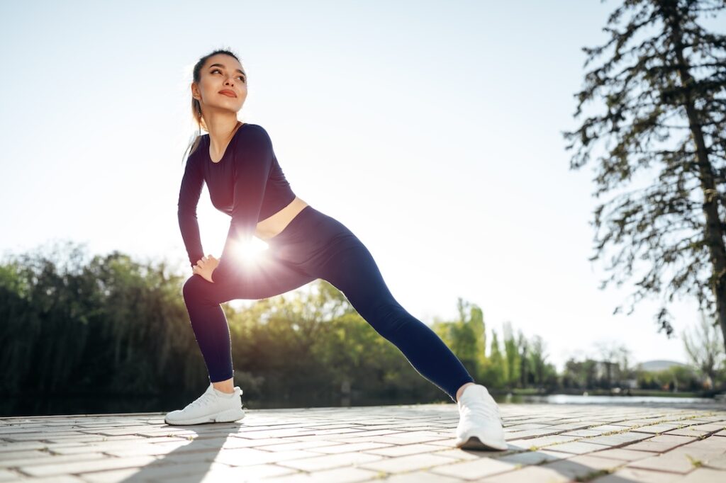 A fit young woman in dark blue sportswear exercises in the morning at the park, experiencing the athletic benefits of NAD+ injections in Muncie, Indiana.