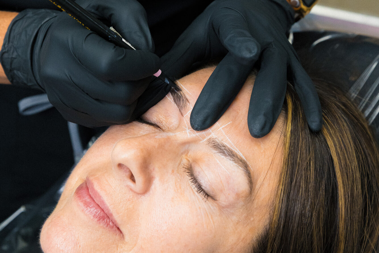 An aesthetician maps out a client's brows for permanent makeup, a treatment popular with patrons of our hair salon near Richmond.